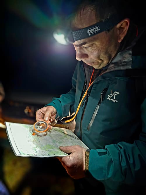 person with a headlamp determines the route on a map with a compass