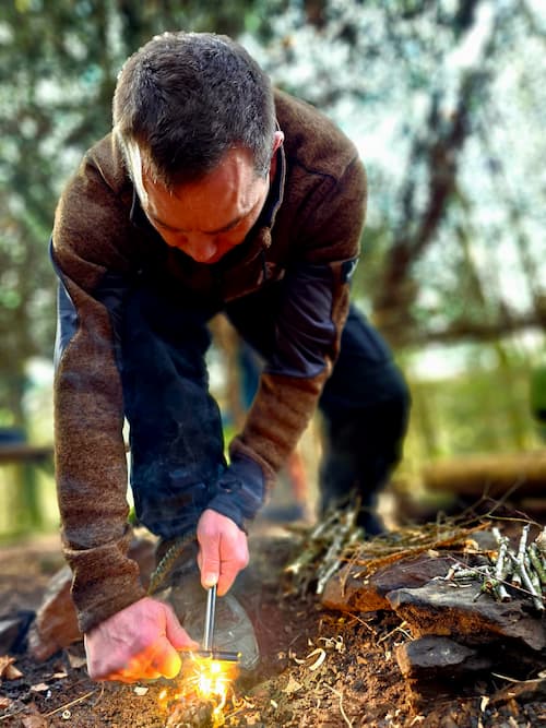 A man sparks a fire using flint and steel during bushcraft training.