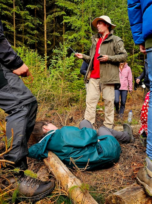 gewond persoon liggend op de grond, staand persoon die instructies geeft