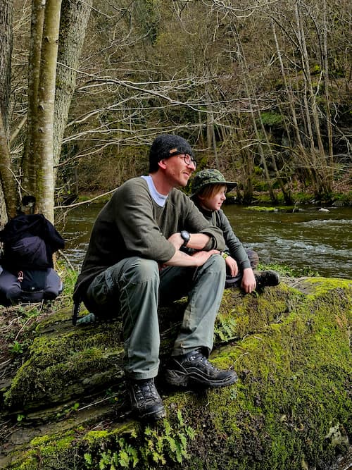 vader en zoon zittend op een boomstam uitkijkend over de rivier